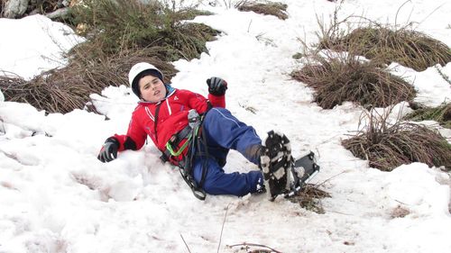 Boy lying in snow covered field by bushes