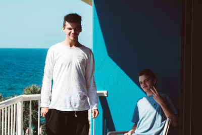 Portrait of male friends at balcony against sea