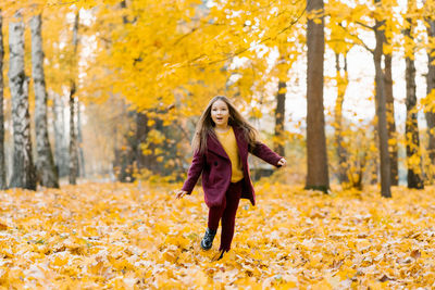 Child girl runs through yellow fallen leaves in an autumn park and laughs