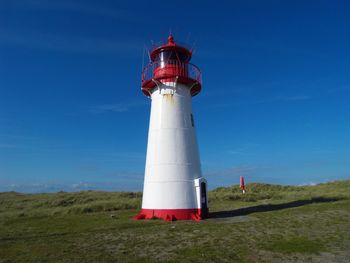 Lighthouse on field by building against sky