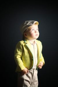 Boy looking away while standing against black background