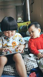 Baby boy sitting with sister using digital tablet on bed