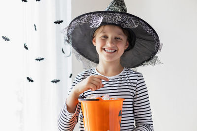 Halloween concept. a girl in a witch hat holds an orange pumpkin bucket with sweets and smiles. 