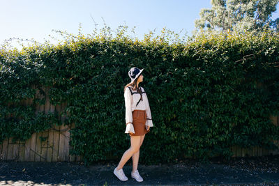 Side view of young woman wearing hat standing against plants in park