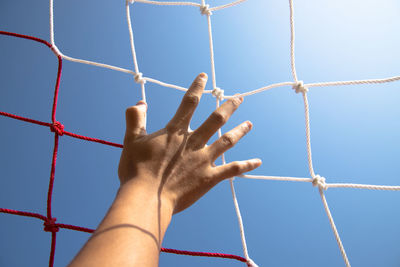 Cropped hand touching soccer net against clear sky