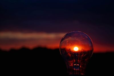 Close-up of illuminated light bulb against sky during sunset