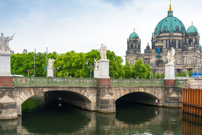 Sculptures on arch bridge over spree river against berlin cathedral