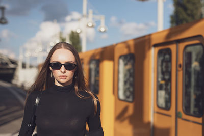 Portrait of young woman wearing sunglasses while standing against train