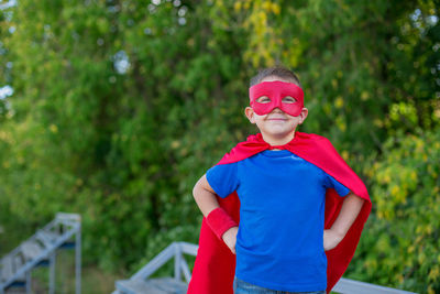 Portrait of boy in superman costume standing against trees