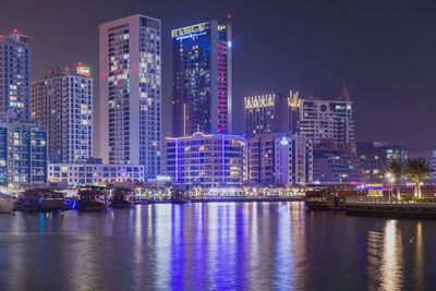 Illuminated buildings by river against sky at night