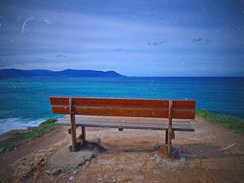 Empty bench on shore by sea against sky