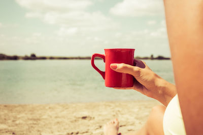 Close-up of woman drinking coffee while relaxing on sandy beach in summer day. copy space.