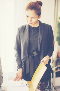 Businesswoman holding file while standing by desk in office