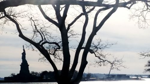 Silhouette bare tree by lake against sky