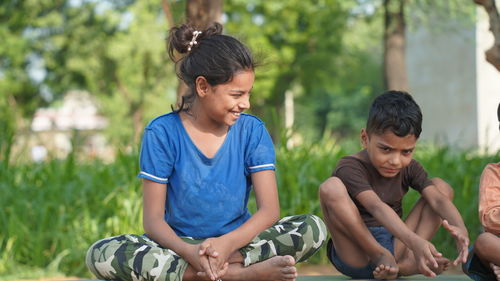 Indian little girl and a boy doing meditate yoga asana on roll mat with eyes closed in park.