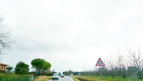 Road sign by trees against sky