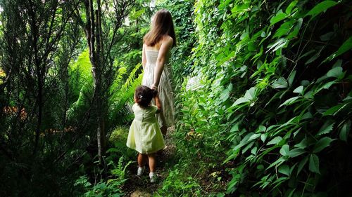 Rear view of woman with daughter standing in forest