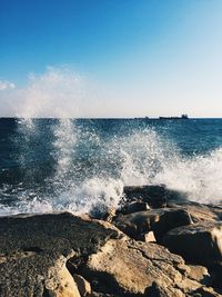 Sea waves splashing on rocks against clear sky