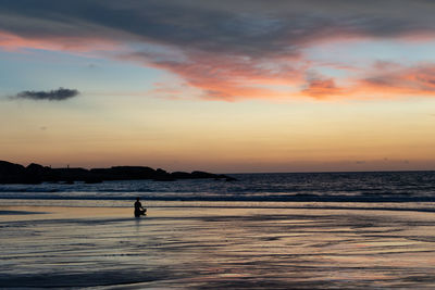 Silhouette person meditating at beach against sky during sunset