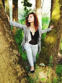 Young woman standing by tree trunk in forest