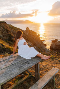 Woman sitting on rock looking at sea during sunset