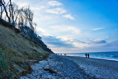 People walking at beach against sky during sunset