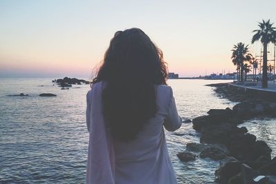 Rear view of woman standing against sea during sunset