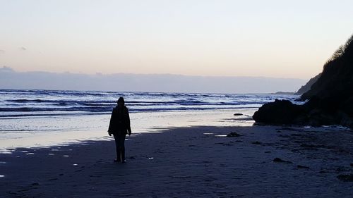 Silhouette friends on beach against clear sky during sunset
