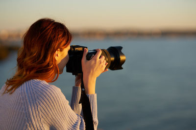 Portrait of woman photographing sea during sunset