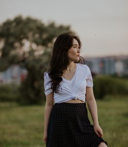 Young woman looking away while standing on field