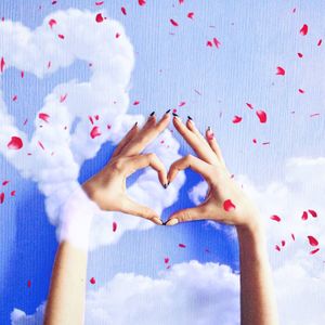 Digital composite image of cropped hands making heart shape in cloudy sky surrounded by petals