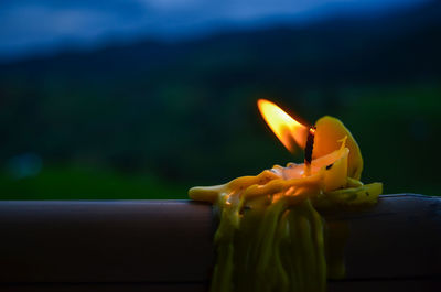 Close-up of illuminated candle melting on railing at dusk