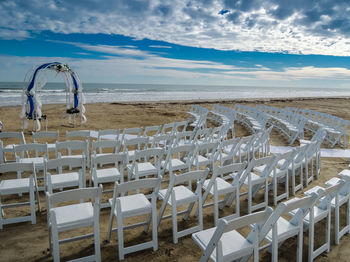 Deck chairs on beach against sky