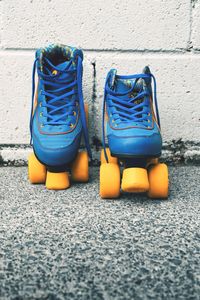 Closeup shot of blue vintage roller skates with orange wheels against white wall