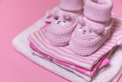 Close-up of baby booties and clothing against pink background