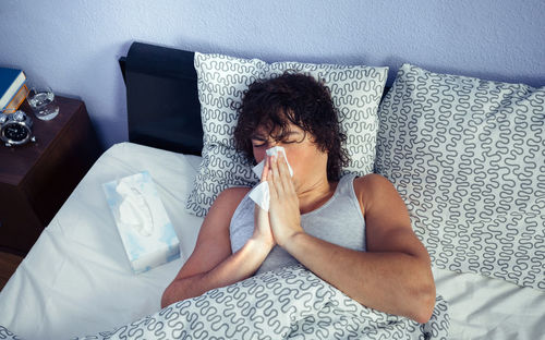 High angle view of young man with flu on bed at home