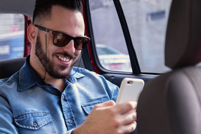 Young man smiling while using phone in car