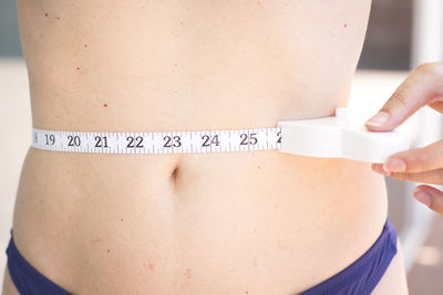 Midsection of shirtless woman measuring waist at home