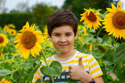 Cute boy stands in sunflower flowers showing a thumbs up