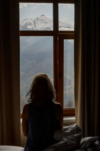 Rear view of woman looking through window at home