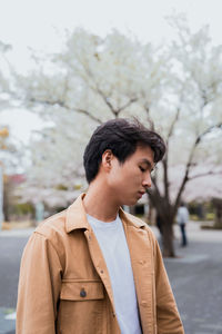 Young man looking away while standing against trees