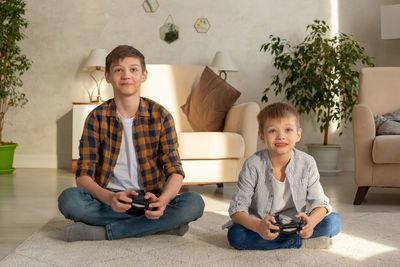 Portrait of two boys sits on the floor in a room playing video games with joysticks