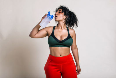 Beautiful young woman drinking water against colored background