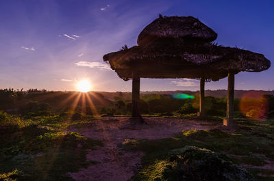 Traditional windmill on landscape against sky at sunset