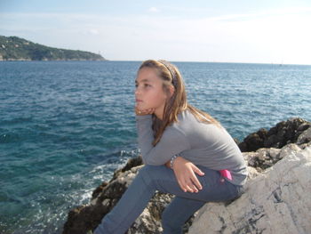 Woman sitting on rock by sea against sky