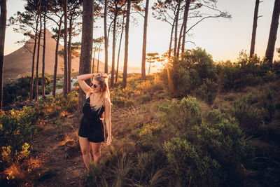 Woman standing against trees during sunset