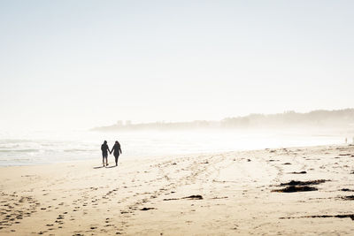 Couple walking on beach against sky