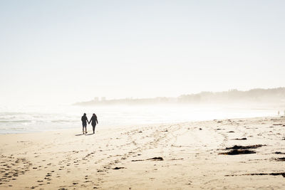 Rear view of men on beach against clear sky