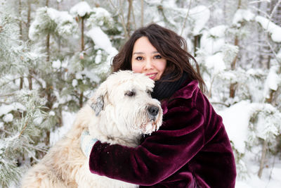 Portrait of smiling woman embracing dog in snow covered forest