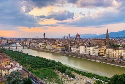 Bridge over river against buildings in city at sunset